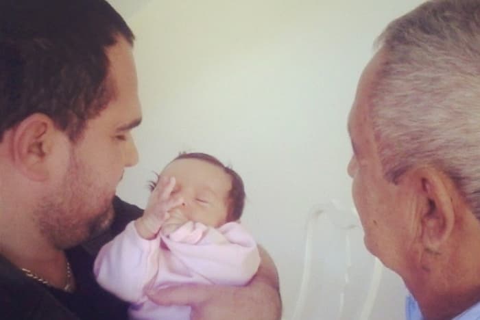 Luciano segurando a neta nos braços ao lado de seu pai, Francisco 