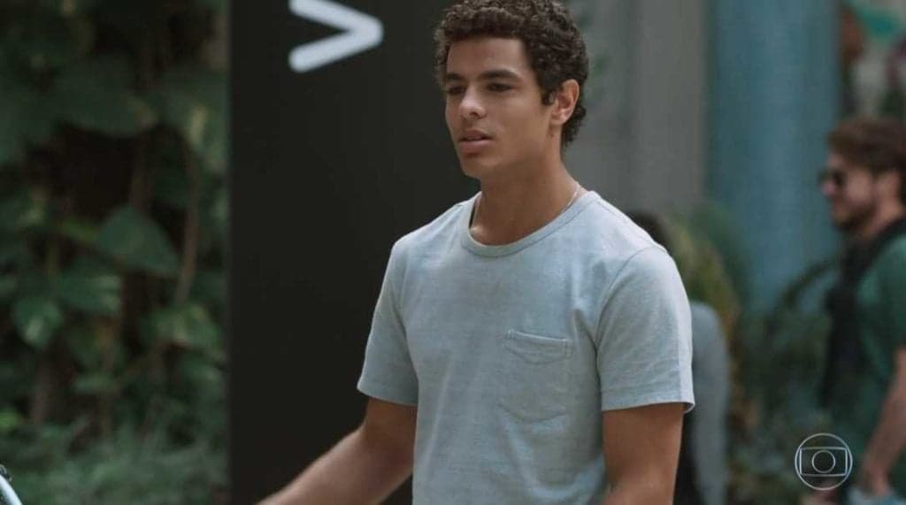 Tato da novela Malhação Viva a Diferença está em pé em área livre de camisa cinza Tato da novela Malhação Viva a Diferença está em pé em área livre de camisa cinza