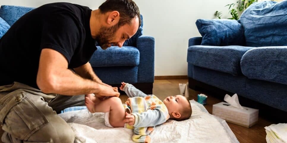 Homem trocando bebê (Foto: Canva)