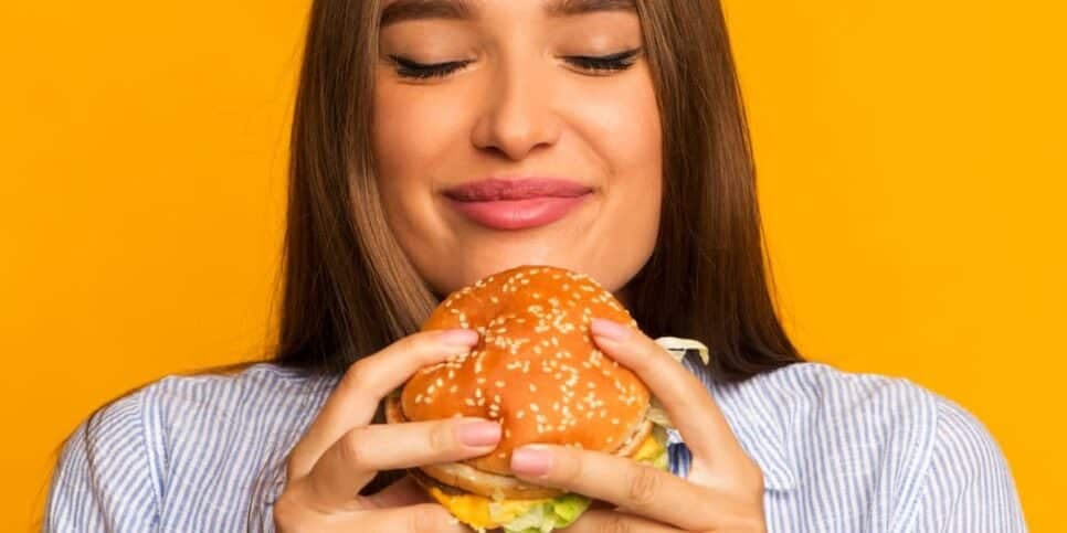 Mulher comendo hambúrguer (Foto: Canva)