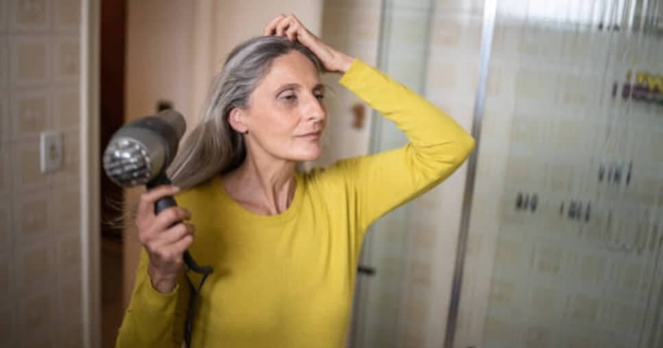 Mulher grisalha secando o cabelo (Foto: iStock)