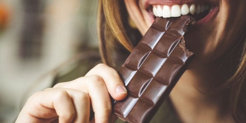 Mulher comendo chocolate (Foto: Canva)