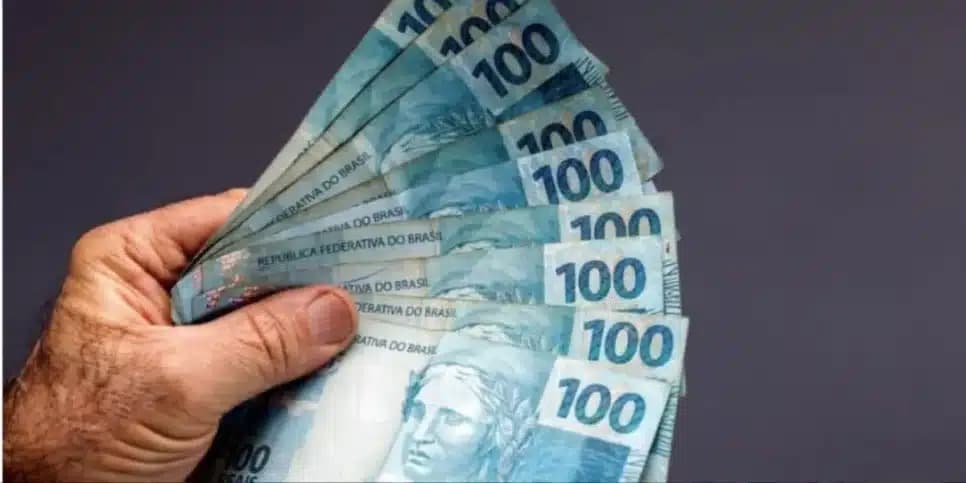 Homem segurando notas de cem reais (Foto: Canva) Homem segurando notas de cem reais (Foto: Canva)