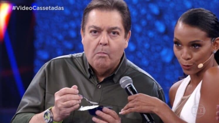 Faustão reclama de fome, devora iogurte ao vivo e tenta se justificar: "Estou aqui desde 10 da manhã''