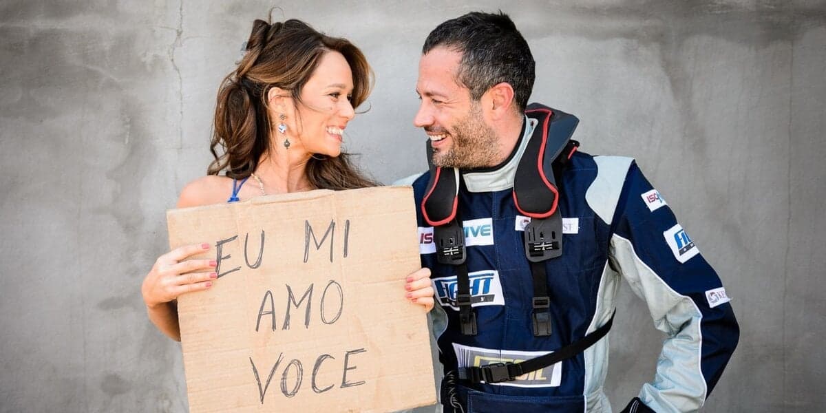 Tancinha e Apolo, vestido de piloto de corrida, se olham sorrindo e ela carrega cartaz escrito "eu mi amo você" em bastidor da novela Haja Coração Tancinha e Apolo, vestido de piloto de corrida, se olham sorrindo e ela carrega cartaz escrito "eu mi amo você" em bastidor da novela Haja Coração