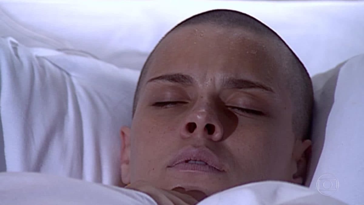 Camila, mulher branca e careca, está deitada com os olhos fechados em cena da novela Laços de Família Camila, mulher branca e careca, está deitada com os olhos fechados em cena da novela Laços de Família