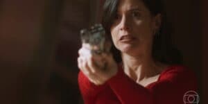 Regina usa vestido vermelho e segura uma arma em cena da novela Cara e Coragem Regina usa vestido vermelho e segura uma arma em cena da novela Cara e Coragem