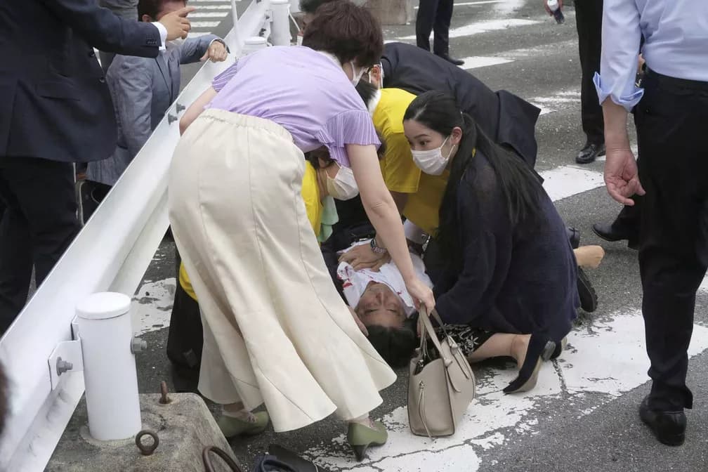 Abe com camisa ensanguentada e mãos no peito caído no chão (Foto: Kyodo / via REUTERS) Abe com camisa ensanguentada e mãos no peito caído no chão (Foto: Kyodo / via REUTERS)