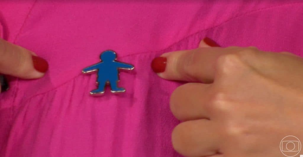Ana Paula Araújo exibiu o broche do Criança Esperança durante o Bom Dia Brasil- Foto: Reprodução/Globo Ana Paula Araújo exibiu o broche do Criança Esperança durante o Bom Dia Brasil- Foto: Reprodução/Globo