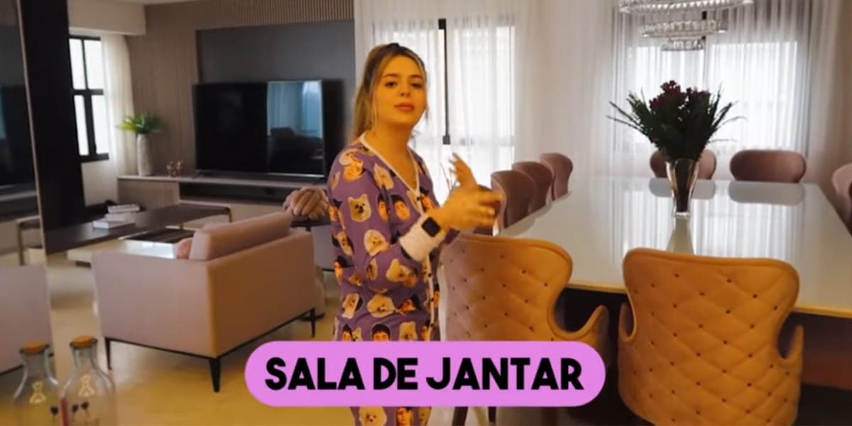 Sala de jantar em conceito aberto e com vista para a sala de estar, com uma grande televisão e sofá confortável (Reprodução: Youtube) Sala de jantar em conceito aberto e com vista para a sala de estar, com uma grande televisão e sofá confortável (Reprodução: Youtube)