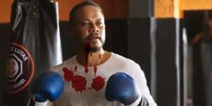 Carlão personagem de Vai na Fé está usando luvas de box azuis, camiseta branca que tem marcas de sangue Carlão personagem de Vai na Fé está usando luvas de box azuis, camiseta branca que tem marcas de sangue