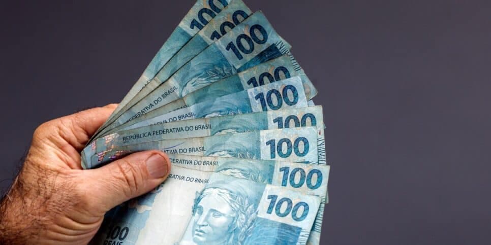 Homem segurando notas de cem reais (Foto: Canva) Homem segurando notas de cem reais (Foto: Canva)